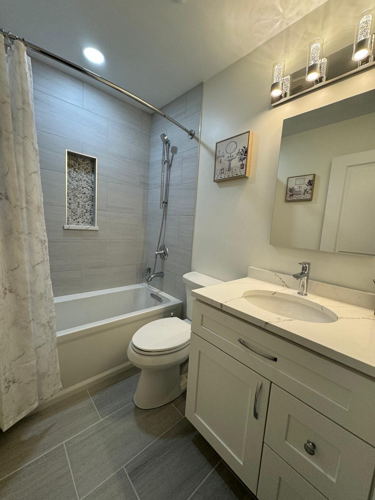 The same bathroom after the remodel, with gray tile tub surround, built-in niche and white vanity