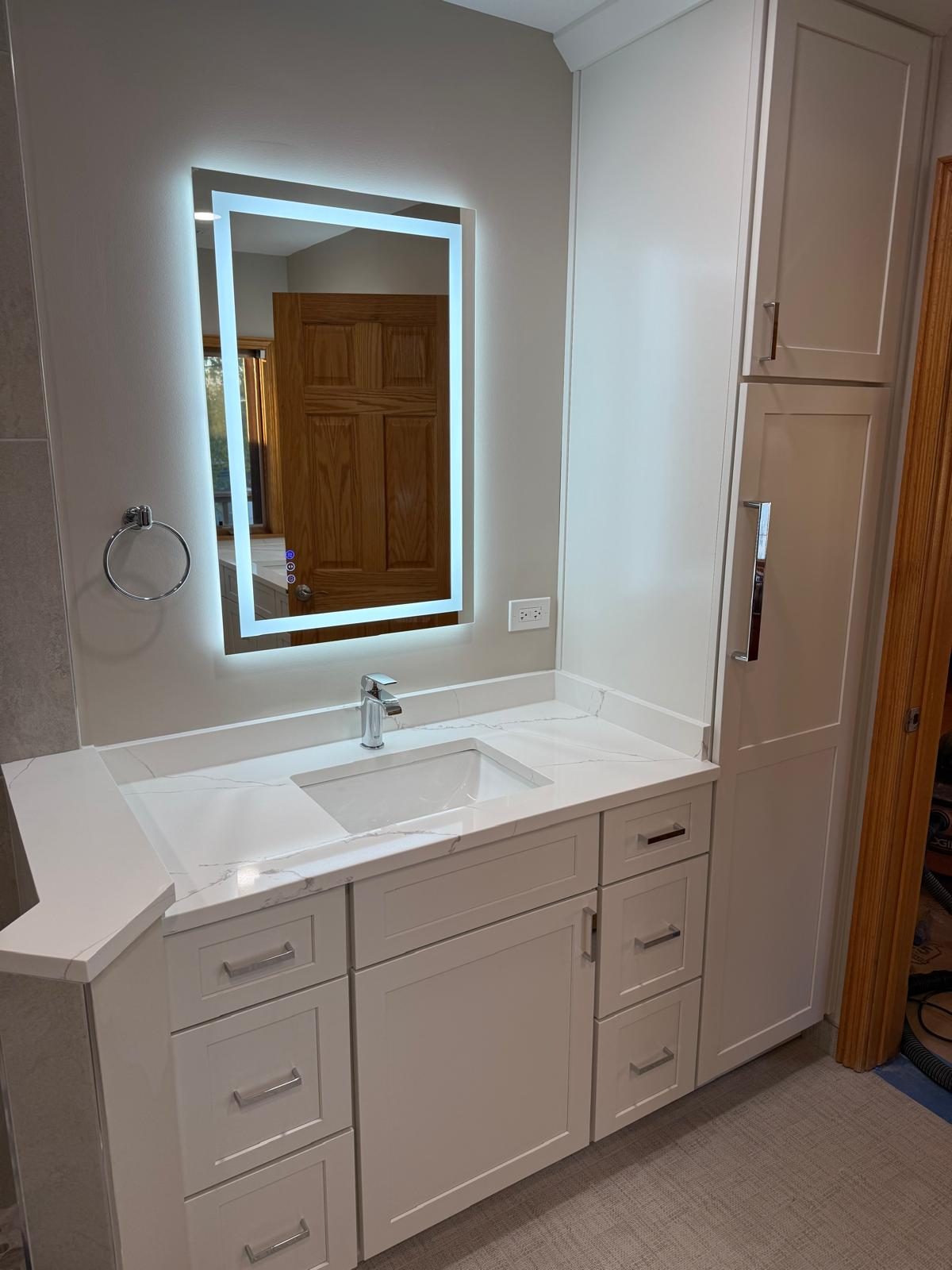 White vanity with LED mirror and a tall linen cabinet