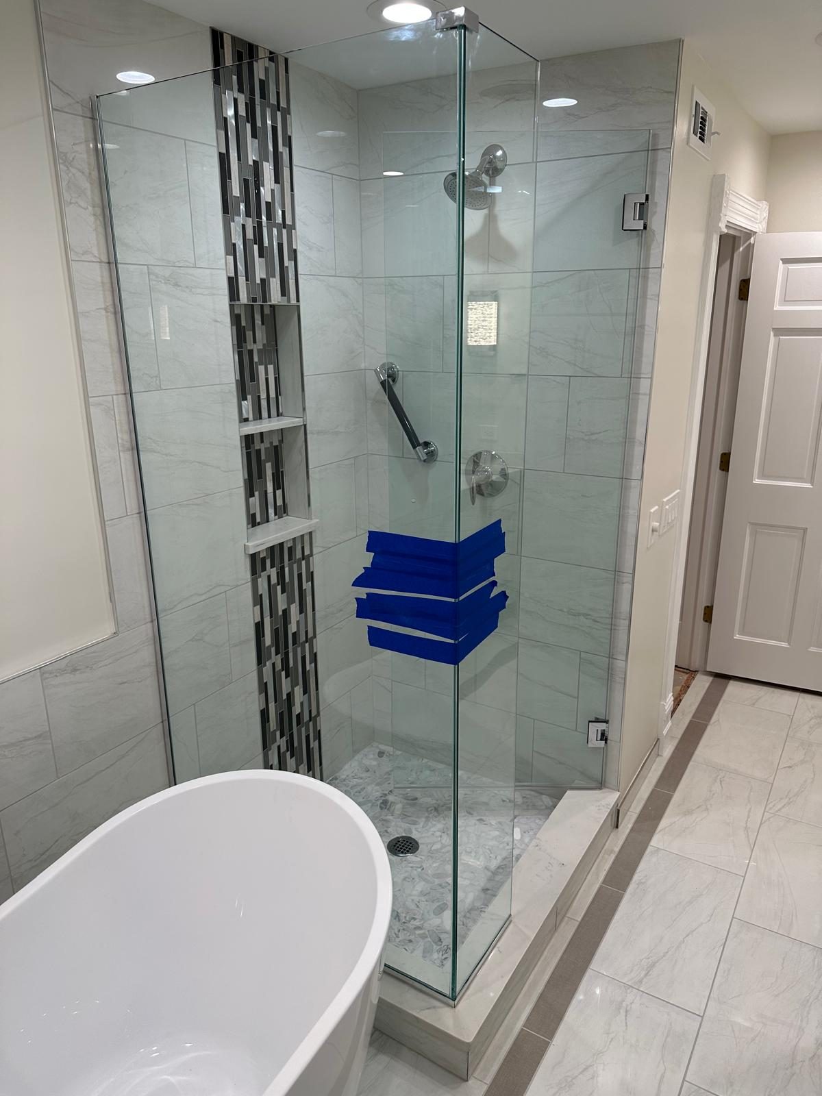 Corner glass shower with marble-look tile, pebble floor and built-in niches