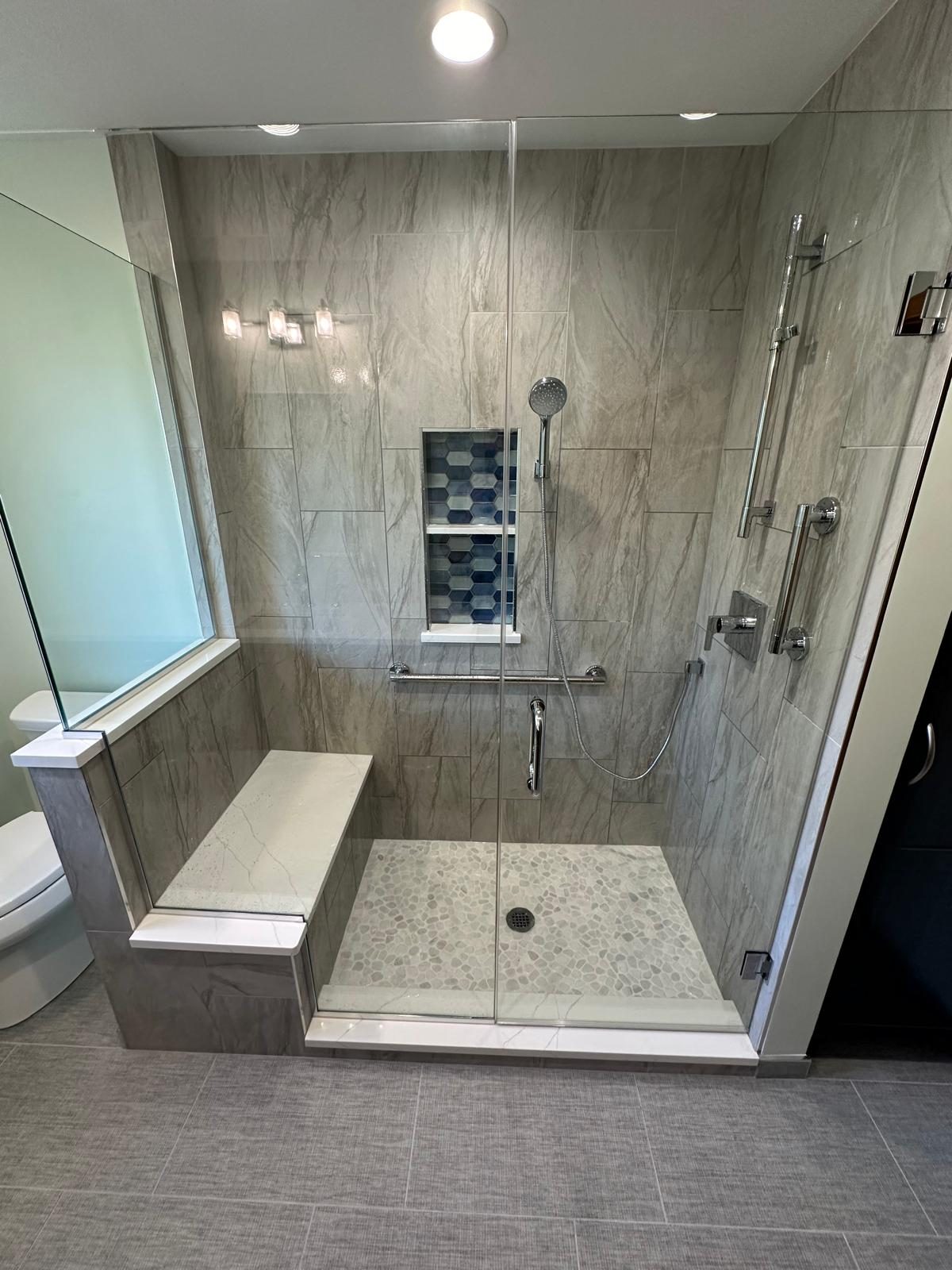 Walk-in shower with glass enclosure, built-in bench, grab bars and a blue tile niche